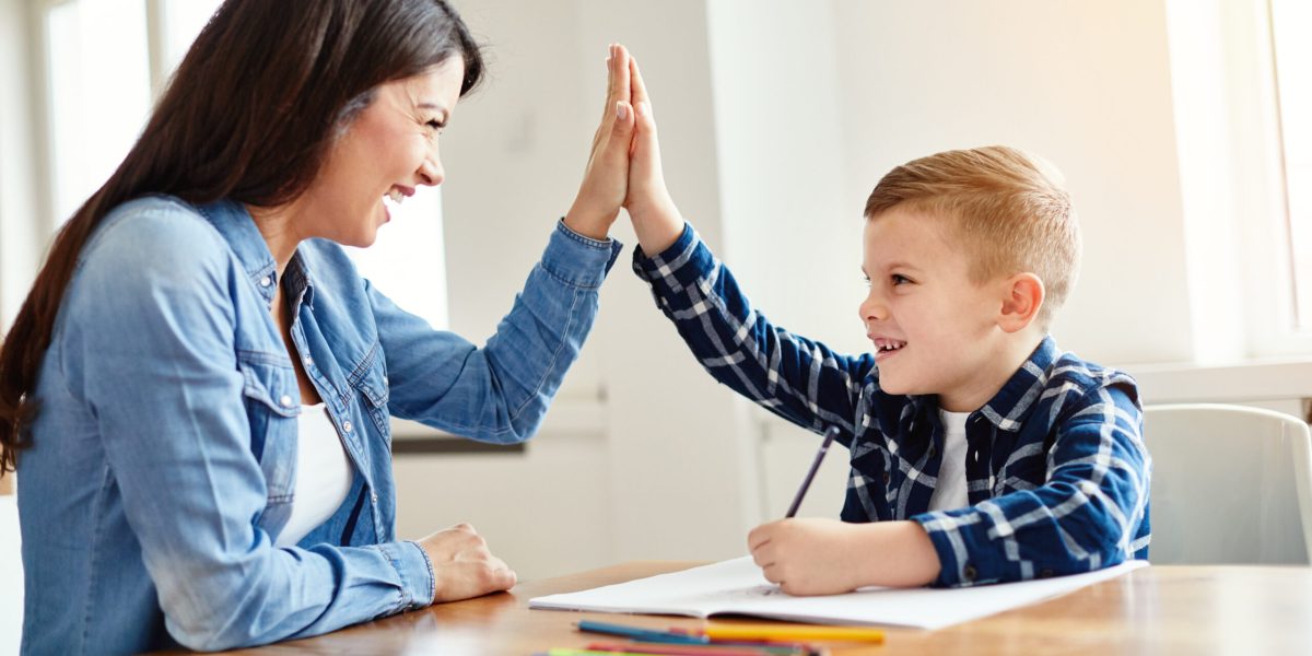 mother teaching son and helping with homework at home, son giving high five to mother